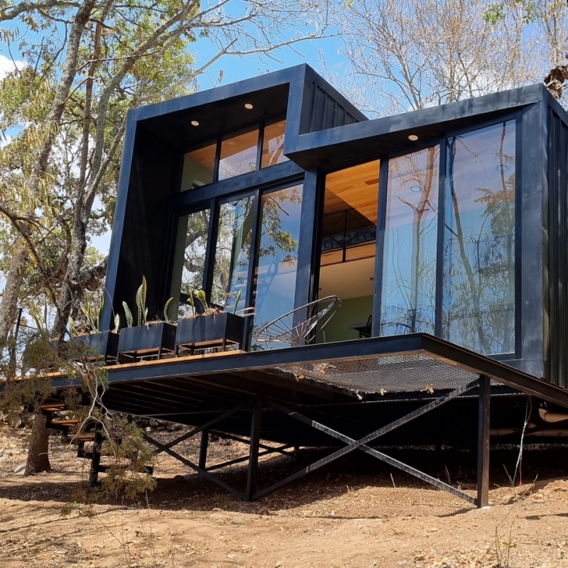 Vista exterior de la fachada de una Tiny House Modelo Nordik 4 equipada con una red para descanso, deck exterior y ventanas panorámicas.